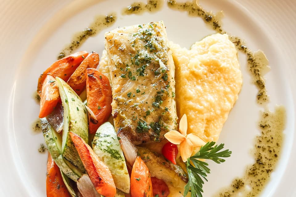 A plated fish course with roasted vegetables and an edible flower