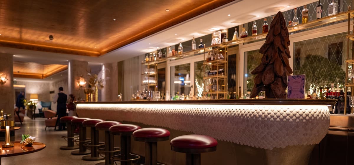 A hotel bar with a sculpted white counter and red leather stools