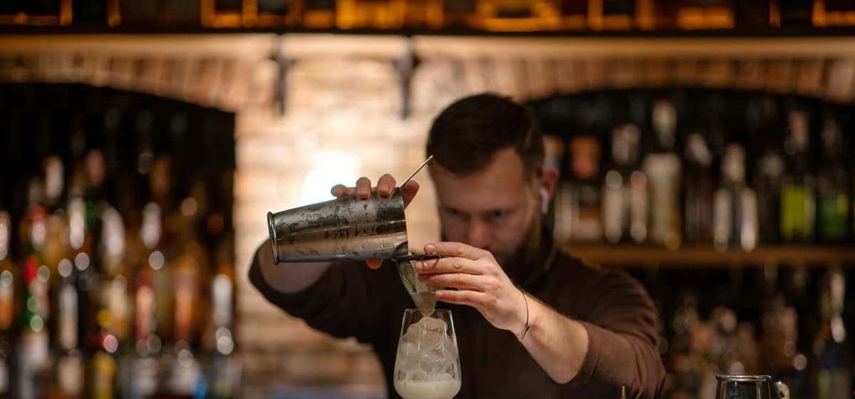 Bartender straining a drink over ice in front of a brick back bar