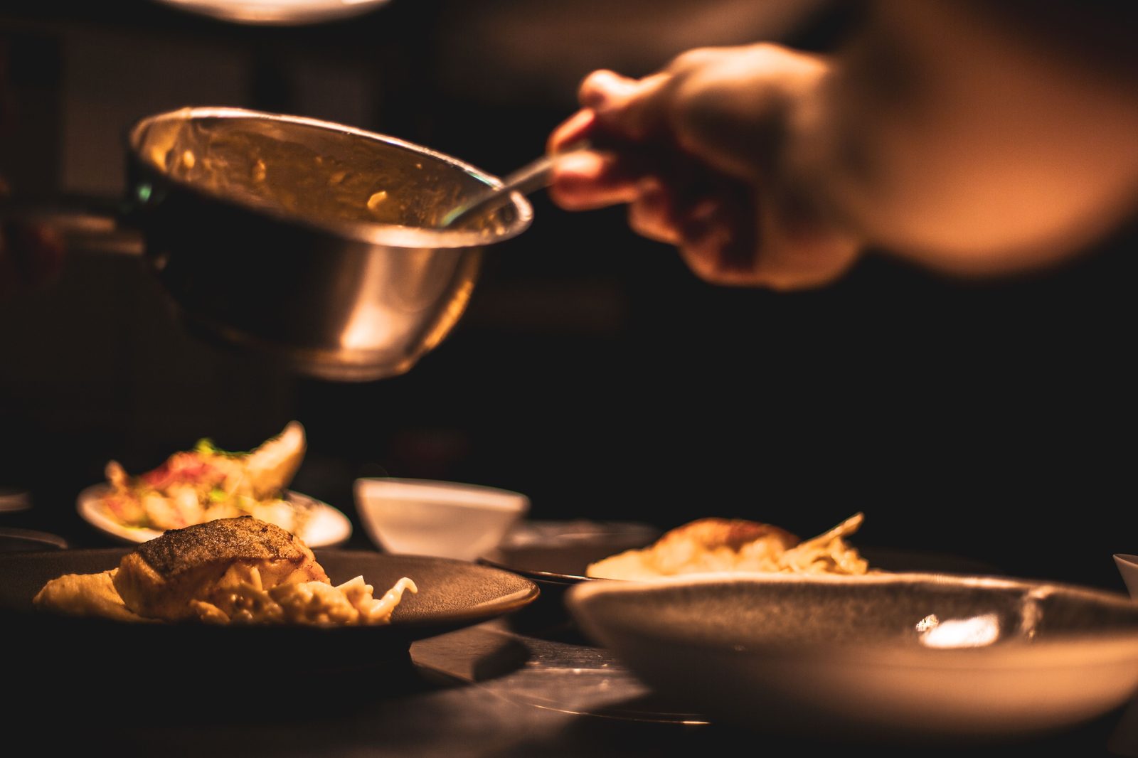 Chef spooning sauce over dishes at the pass