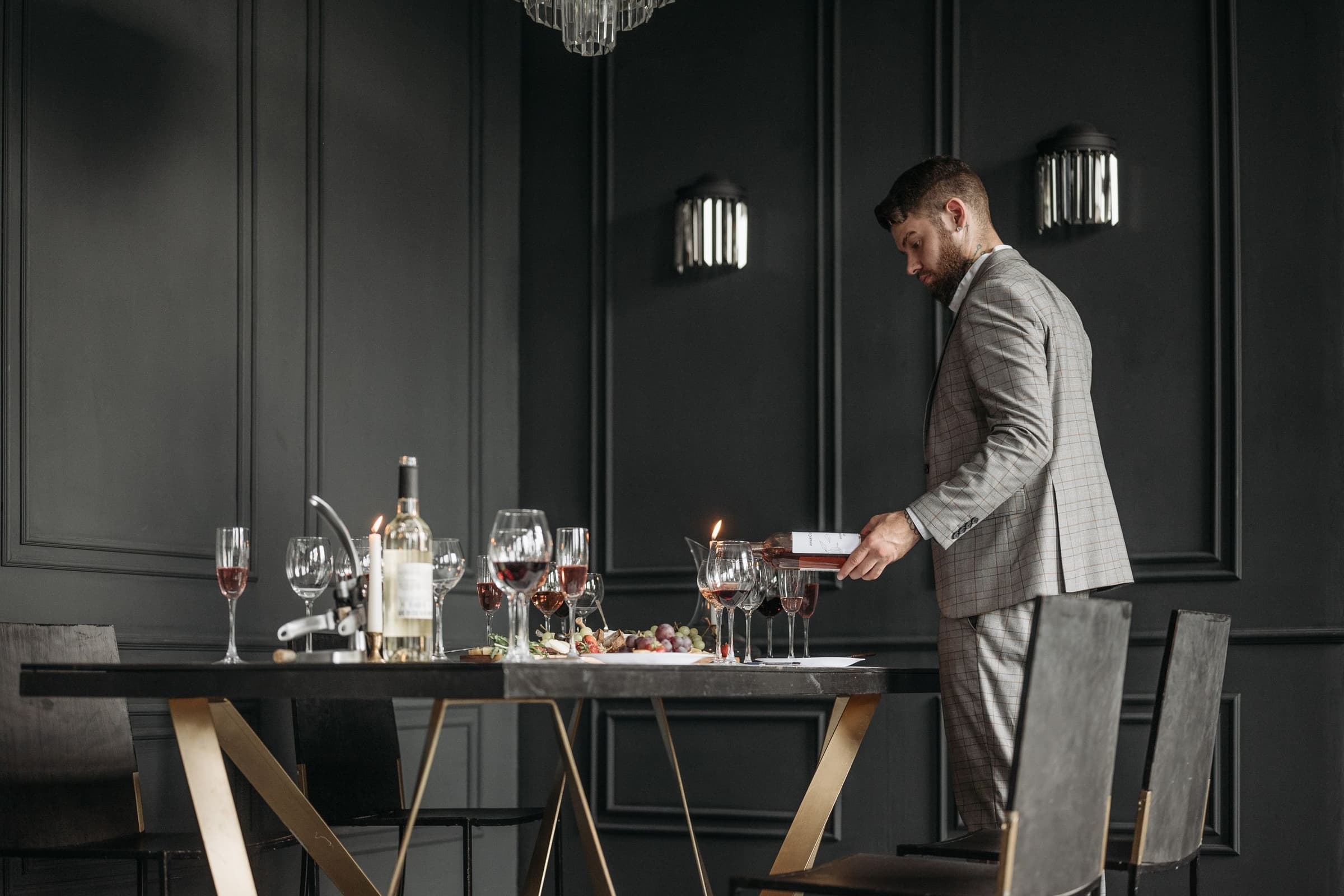 A manager in a check suit pouring wine at a set table in a dark panelled dining room