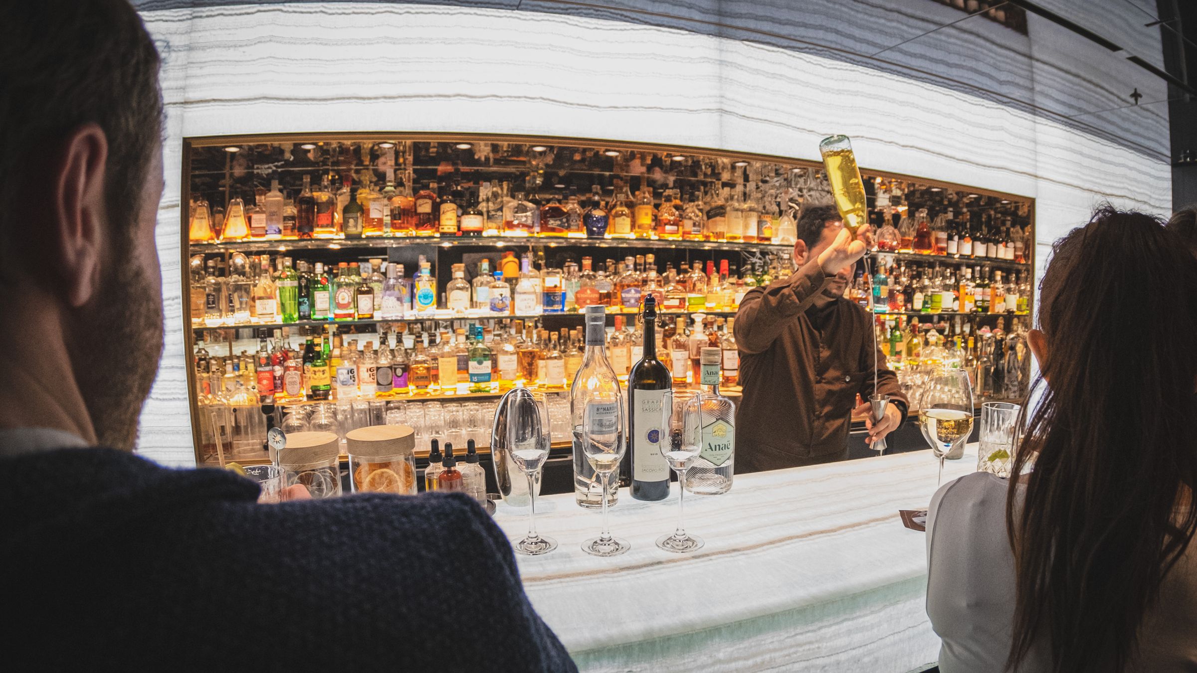 Bartender working a back bar lined with bottles while guests look on