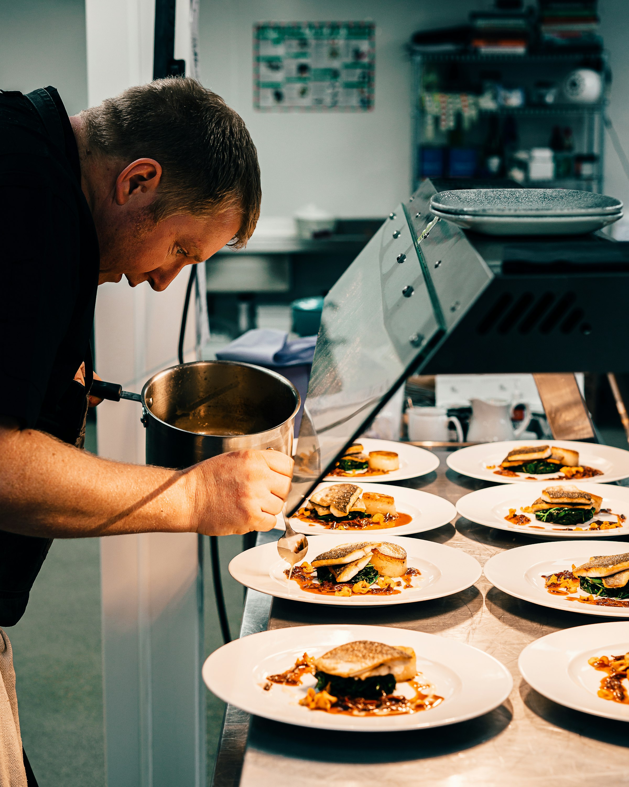 Chef saucing a row of plates at the pass